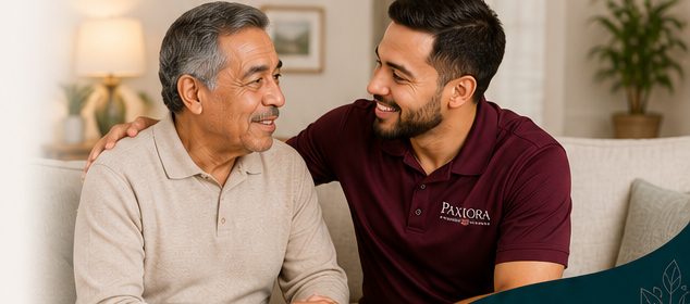 A Hispanic caregiver with his arm around an older Hispanic man, both smiling