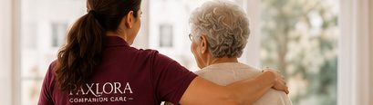 A caregiver with her arm around an older woman, looking out a window together